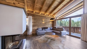A modern living room with a wooden ceiling, a fireplace, a sofa, and a large window with a mountain view. - Chalet in Neukirchen near Anfängerpiste (Neukirchen)