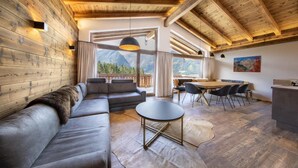 A modern interior with a wooden ceiling, a sofa, a dining table with chairs, and a view of mountains through large windows. - Chalet in Neukirchen near Anfängerpiste (Neukirchen)