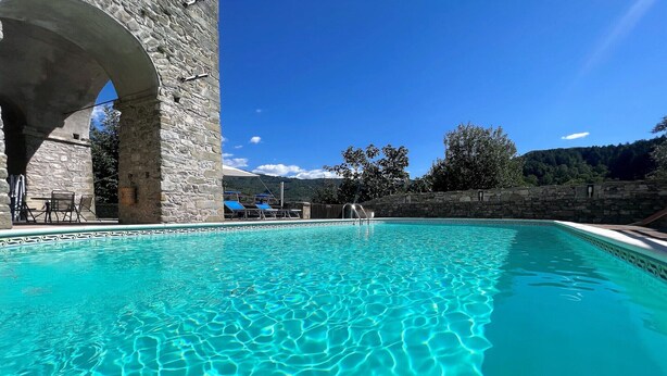 A clear blue pool with a stone wall and an archway.