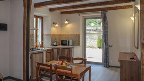 A kitchen with wooden beams, a dining table with chairs, a microwave, and a window with curtains.