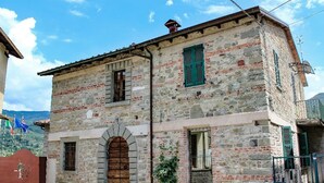 A stone building with a wooden door and green shutters, featuring a small arched entrance and a visible balcony.