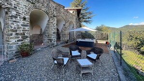 A stone building with arched doorways, outdoor seating with chairs and a table, and a hot tub.
