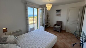 A bedroom with a bed, a chair, a glass table, a door, and a view of the outdoors. - Superb villa with sea view and private pool (MONTICELLO)
