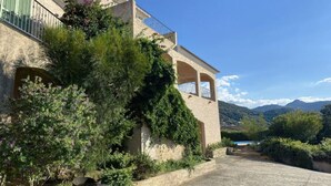 A Mediterranean-style building with a stone facade, arched windows, and a balcony overlooking a mountainous landscape. - Superb villa with sea view and private pool (MONTICELLO)