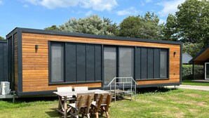 A modern, single-story building with a wooden exterior and large windows. - Tiny House in Netherlands with Garden (Lathum)