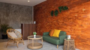 Un vestíbulo con un sofá verde, una silla de mimbre y mesas redondas.