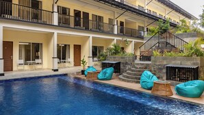 Un hotel con piscina, mobiliario exterior y una construcción de varios pisos con balcones.