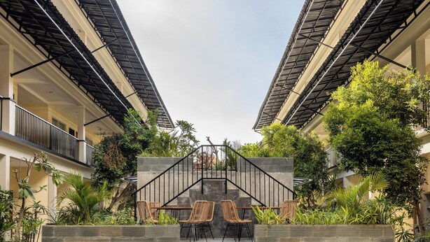 Un patio con una escalera central, rodeado de mobiliario exterior y abundante vegetación.