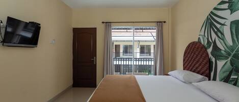 A hotel room with a bed, a television mounted on the wall, a door, and a window with curtains.