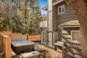 A hot tub in a backyard with a wooden deck and a tree.