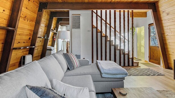 A cozy cabin interior with a wooden staircase, a gray sectional sofa, and a small table.