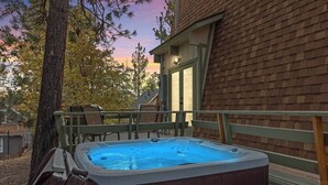 A hot tub outside a house with a wooden deck and chairs.