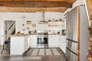 A modern kitchen with white cabinets, stainless steel appliances, and a wooden ceiling.