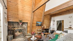 Ein gemütliches Blockhaus-Interieur mit Kamin, einer Couch, einem Fernseher und einer Treppe, die nach oben führt.