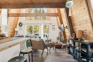 A cozy loft-style room with a high ceiling, wooden beams, a dining area, and a kitchen with a black countertop.