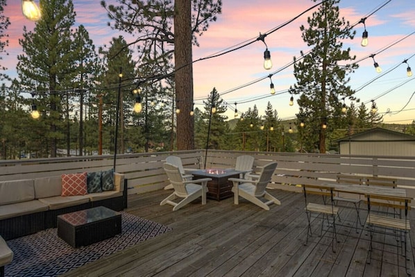 A deck with outdoor seating, a fire pit, and string lights.