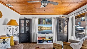 A cozy living room with a wooden ceiling, a television, and a view of a lake through a window.