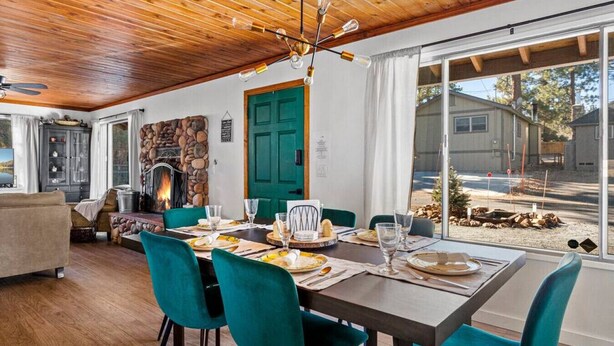 A dining area with a stone fireplace, teal chairs, and a wooden ceiling.