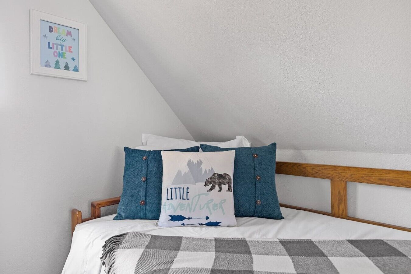 Ein Schlafzimmer mit einem hölzernen Kopfteil, einer karierten Tagesdecke und dekorativen Kissen mit einem Bären-und-Pfeil-Muster.