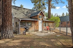 A cabin with a front porch, a grill, and a dining area with chairs.