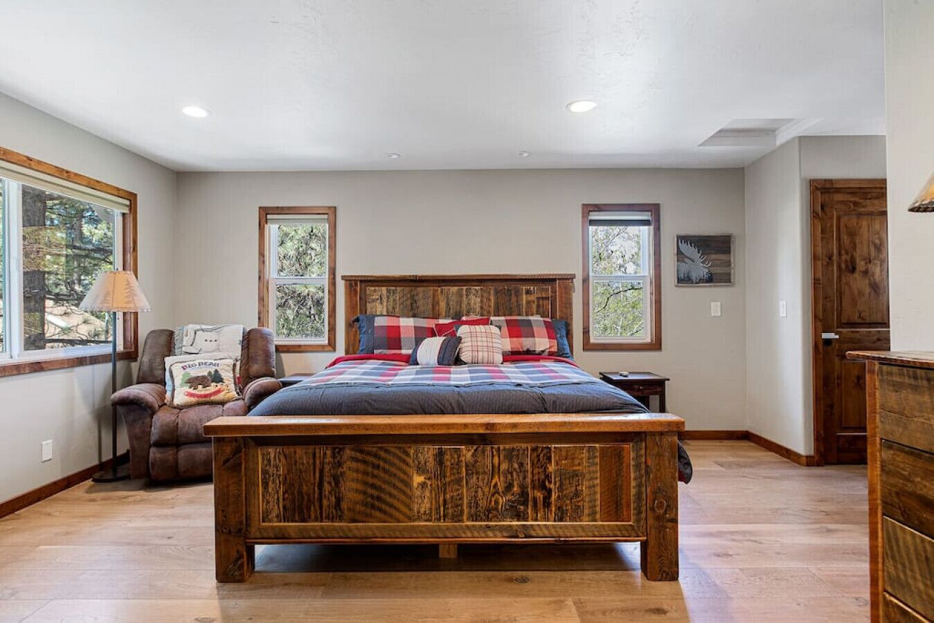 Un dormitorio amplio con una cama de madera grande, dos ventanas, una silla y un aparador.
