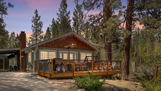A cabin with a deck, surrounded by tall trees and a clear sky.