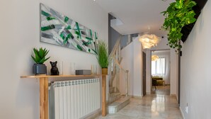 A modern hallway with a marble floor, a wooden console table with plants, a radiator, and a staircase with a light fixture. - Lagom Hotel (Bucharest)