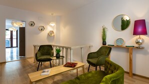 A modern living room with green velvet sofas, a wooden coffee table, and a small side table with a plant. There is a round mirror and a clock on the wall, and a wooden console table with a lamp. - Lagom Hotel (Bucharest)