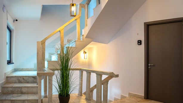 A marble staircase with a white railing, a potted plant, and a door with a number plate. - Lagom Hotel (Bucharest)