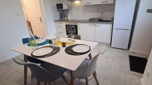 Un comedor con una mesa dispuesta para dos personas, una cocina al fondo y una puerta blanca.