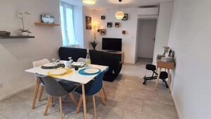 Un comedor con una mesa dispuesta para cuatro personas, un sofá negro y un televisor al fondo.