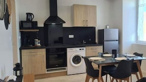 Una cocina compacta con lavadora, microondas y refrigerador. Hay una mesa de comedor con sillas.