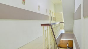 A clean, well-lit hallway with a wooden handrail, a tiled floor, and a small kitchenette area with cabinets and a sink.