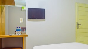 A hotel room with a bed, a desk with a mirror, a television, and a door.