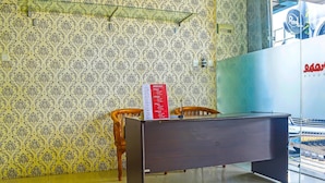 A reception desk with a patterned wallpaper, a wooden chair, and a glass partition.