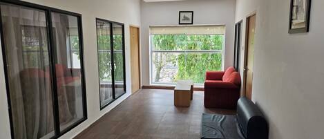 A spacious living room with large windows, a ceiling fan, and a red sofa.