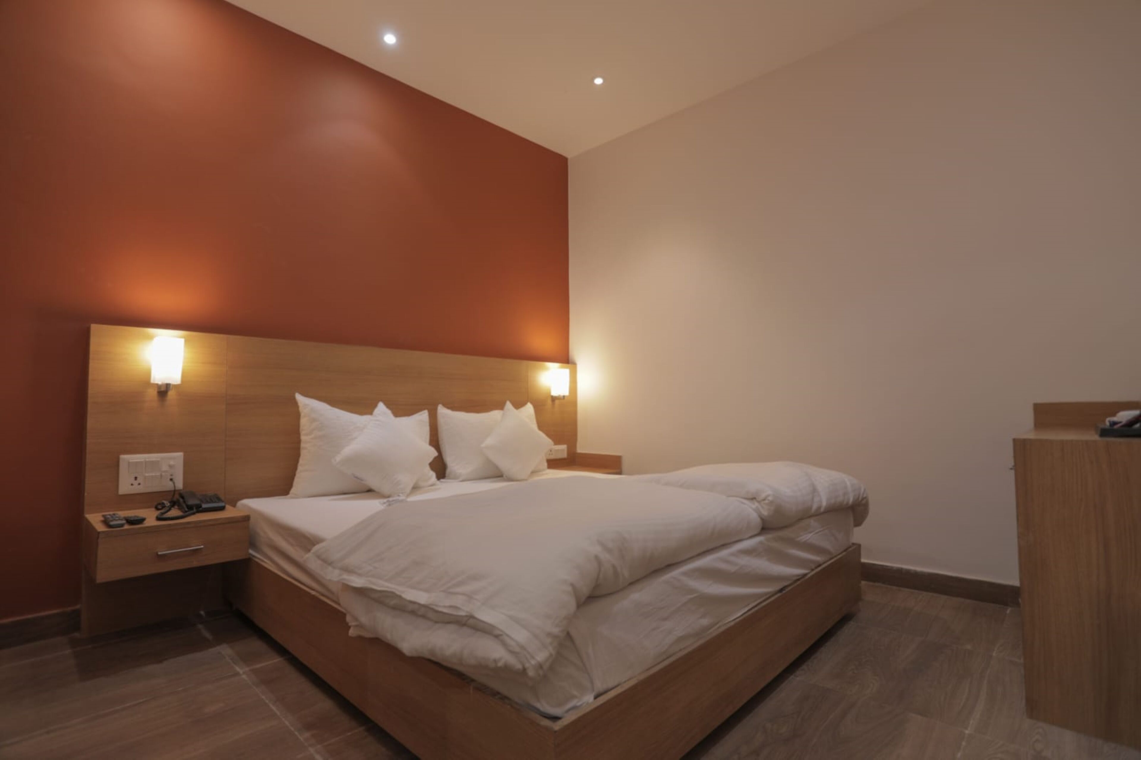 Habitació d'hotel moderna amb un llit de fusta, dues taules de nit i una petita taula auxiliar.