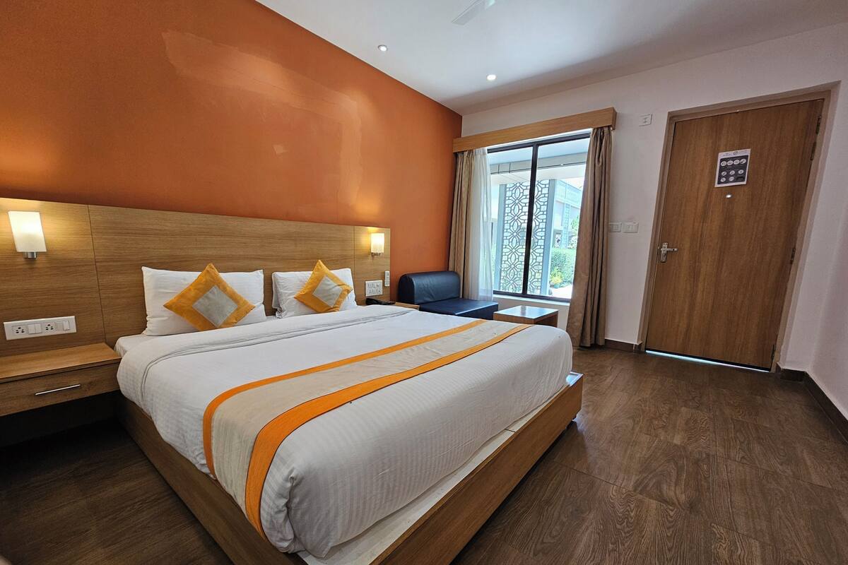 A hotel room with a large bed, wooden headboard, and a view of the outside through a window.