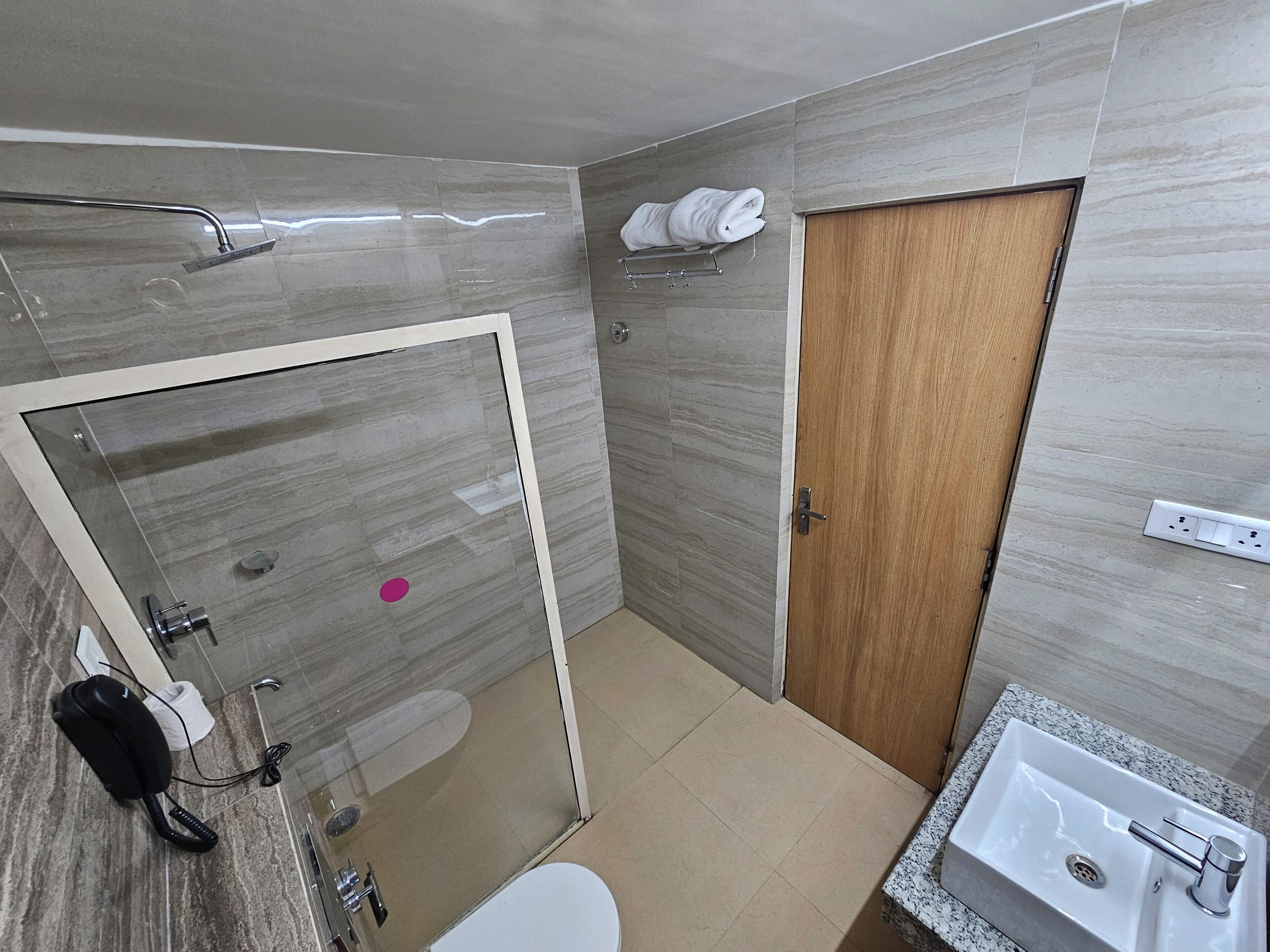 A modern bathroom with a glass-enclosed shower, a wooden door, and a sink with a marble countertop.