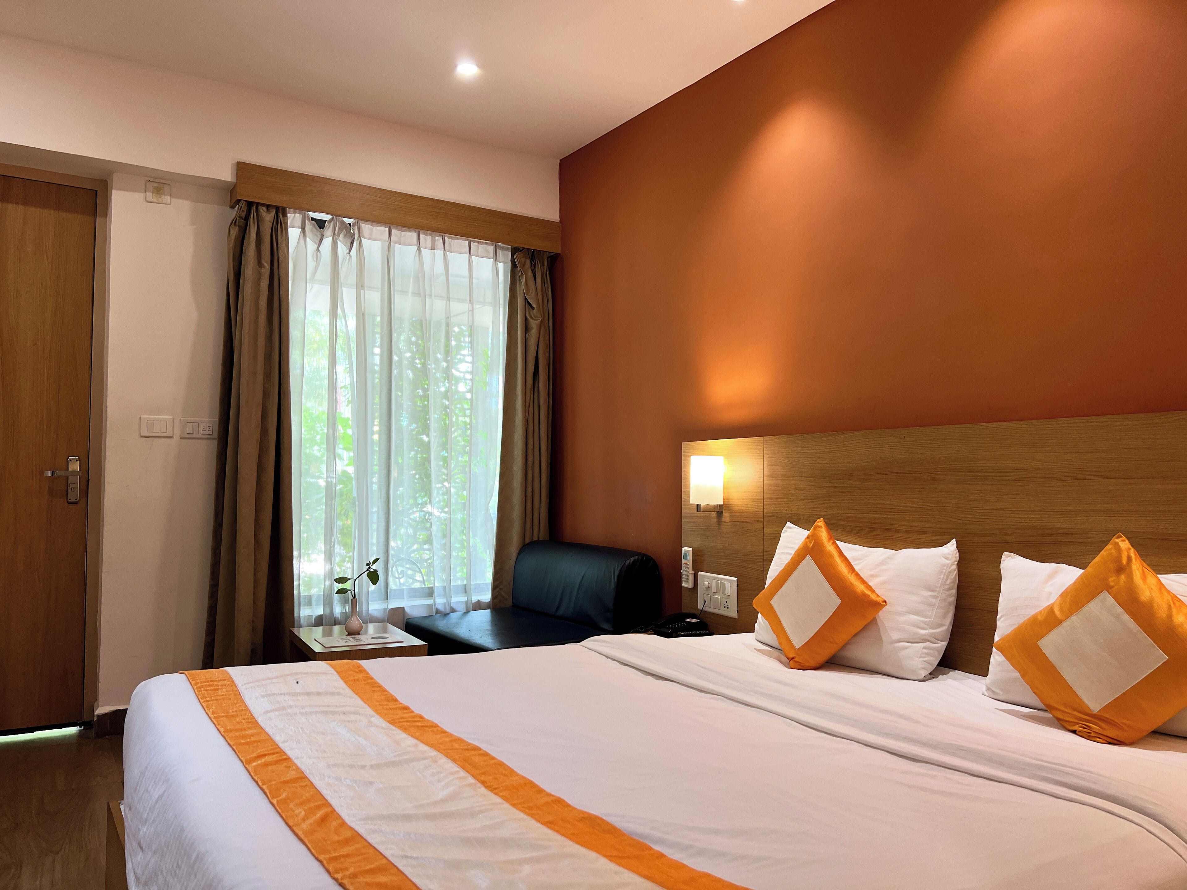 A hotel room with a bed, a nightstand, a lamp, a chair, and a window with curtains.