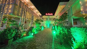 A hotel with a sign reading "The Bundela" at night, featuring illuminated string lights and a paved walkway.