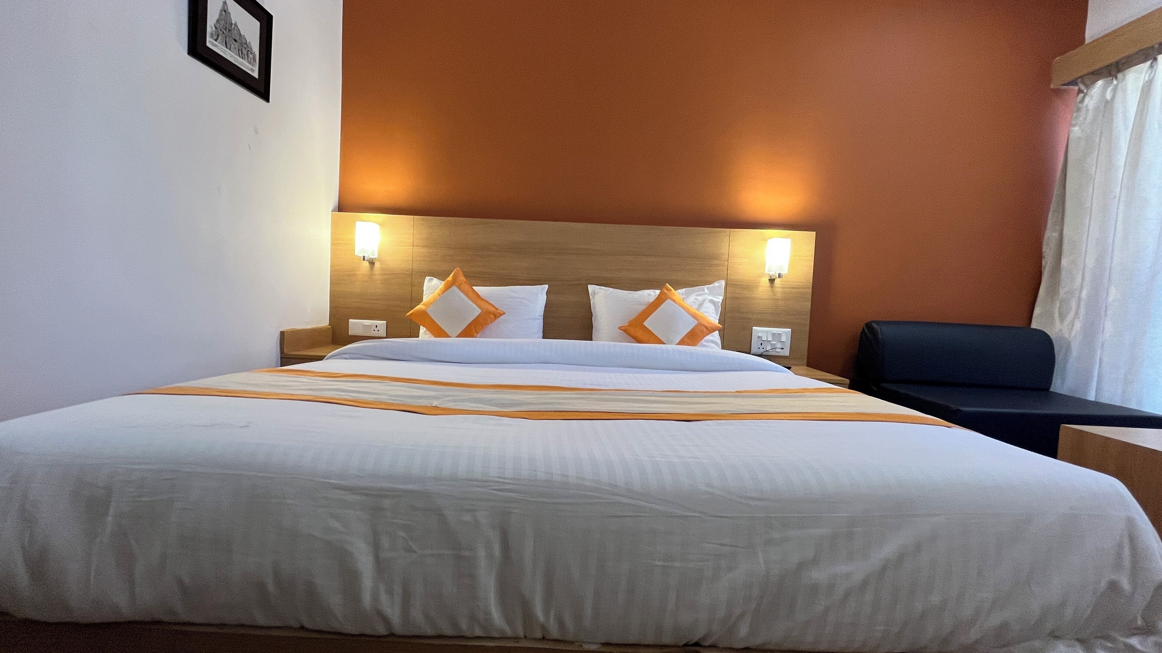 A hotel room with a large bed, two wall-mounted lights, a wooden headboard, and a black chair.