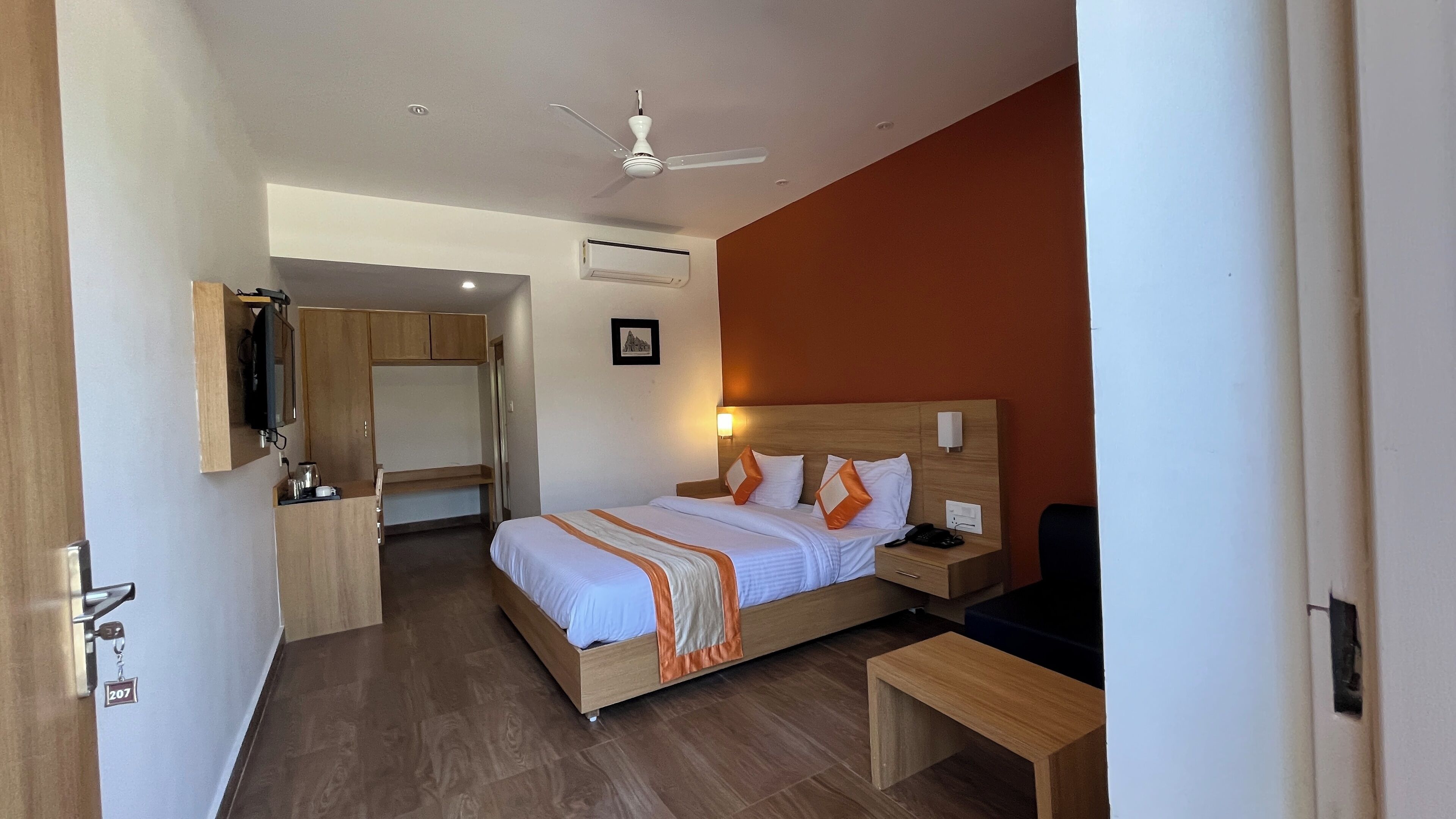 A hotel room with a bed, bedside table, desk, and a ceiling fan.