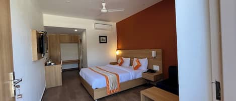 A hotel room with a bed, bedside table, desk, and a ceiling fan.