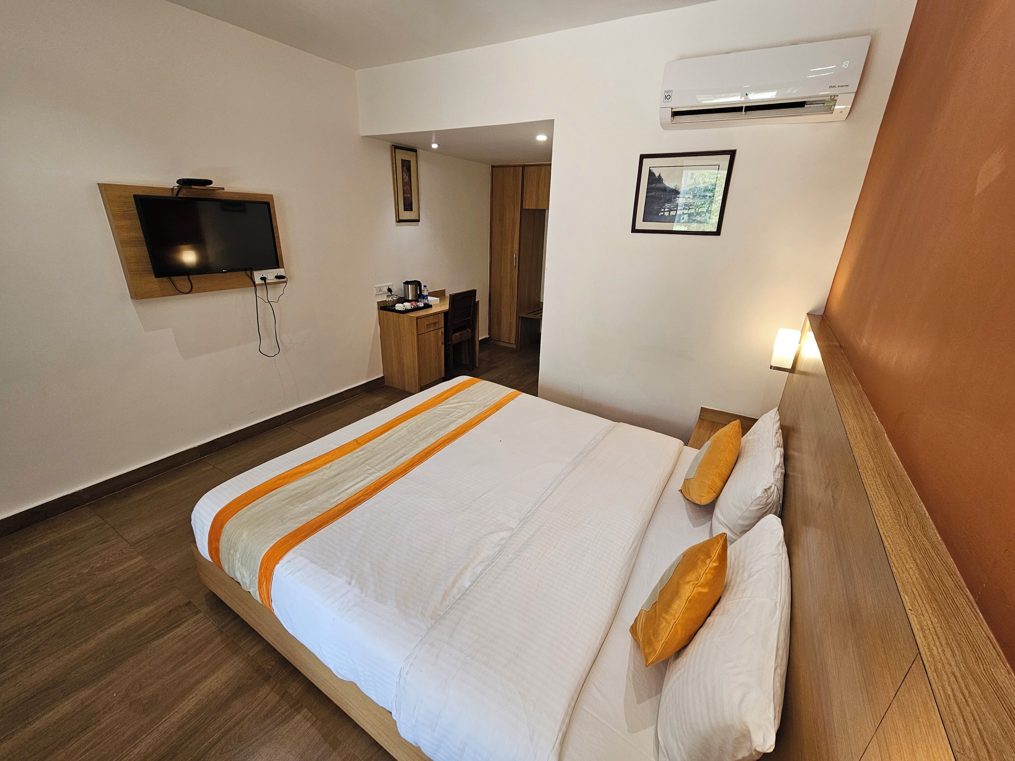 A hotel room with a bed, a desk, a television, and an air conditioning unit.