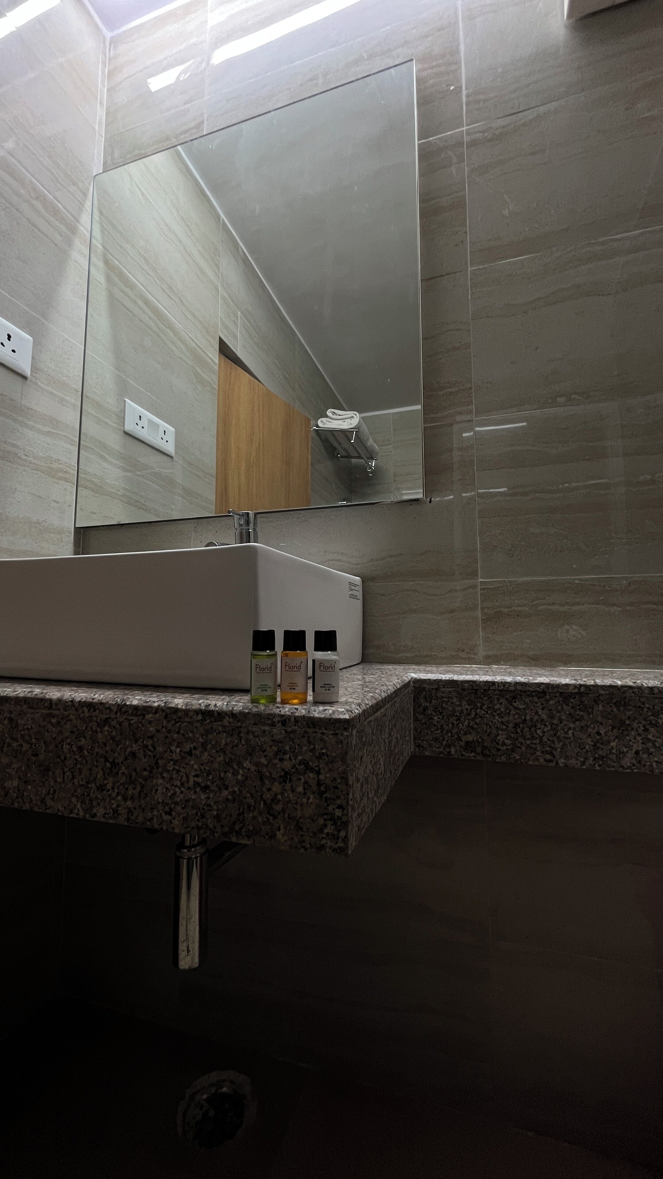Un bagno moderno con un piano in granito, un lavandino bianco e uno specchio sopra. Sul piano del lavabo ci sono tre flaconi di sapone per le mani.