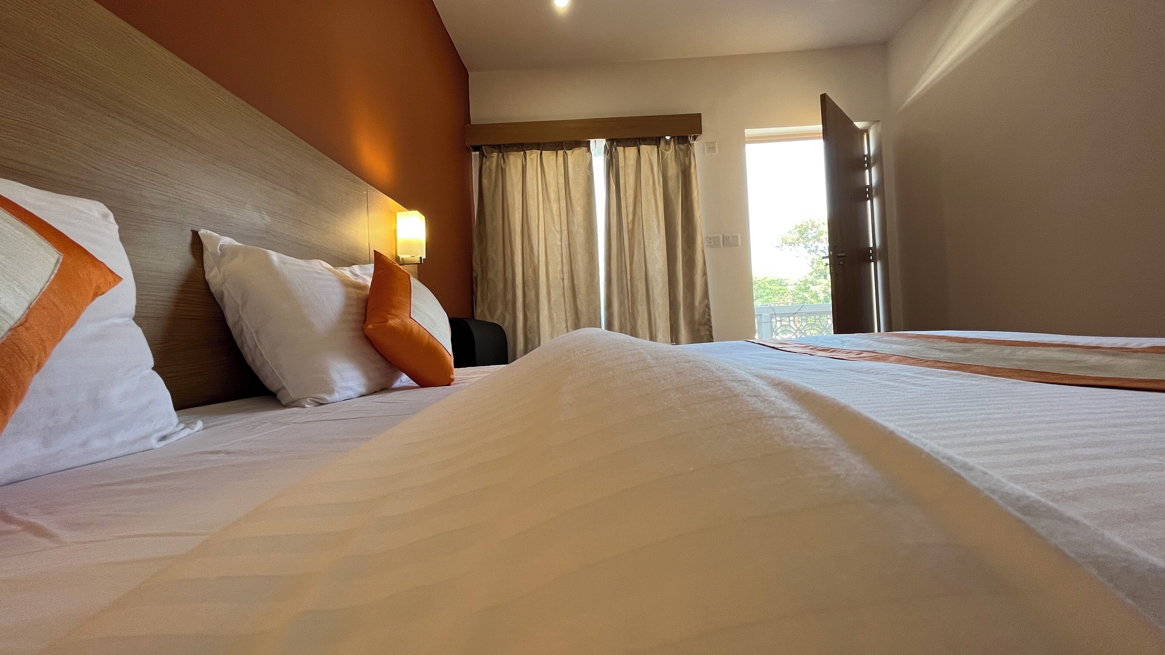 Ein Hotelzimmer mit Bett, Nachttisch, Lampe und Blick ins Freie durch ein Fenster.
