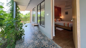 A modern hotel room with a large bed, a bedside table, and a view of greenery outside.