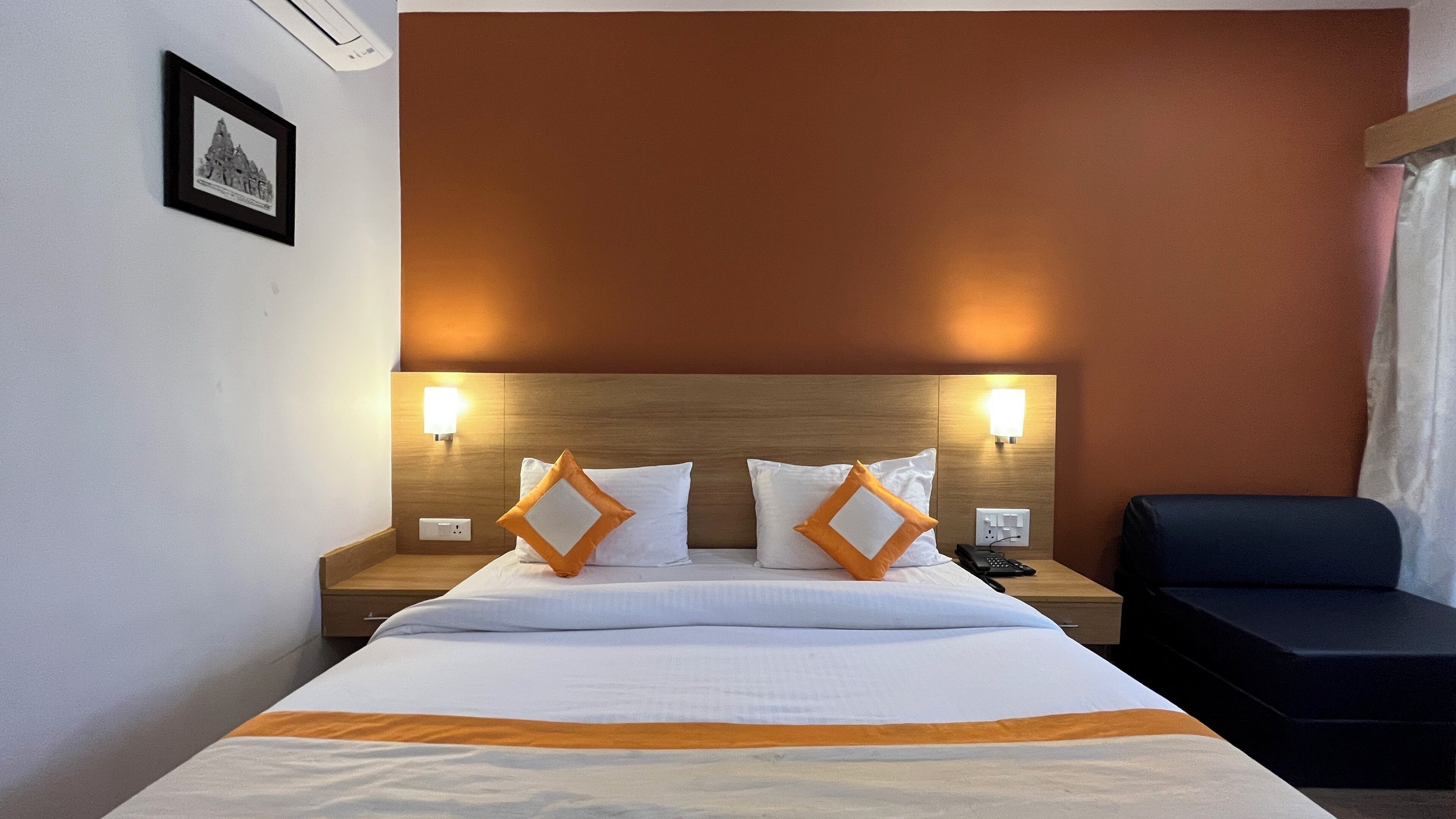 A hotel room with a large bed, two bedside tables with lamps, a black chair, and a framed picture on the wall.