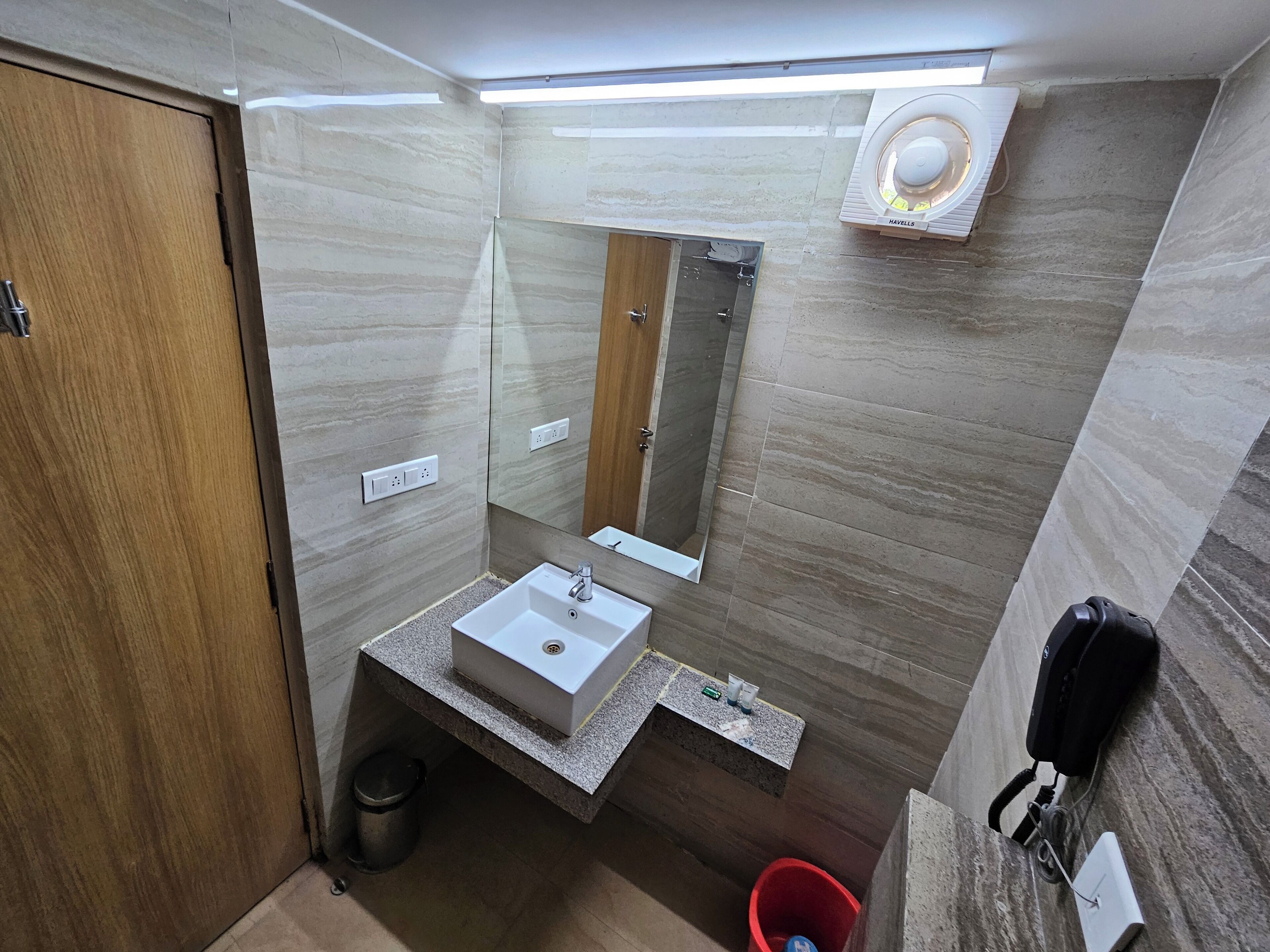 Een moderne badkamer met een houten deur, een witte wastafel, een spiegel en een douche.